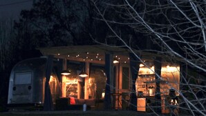 A covered outdoor area with a dining table and chairs, a small seating area, and a kitchen area with a stove and sink. - Hocking Hills Airstream & Outdoor Living (McArthur)