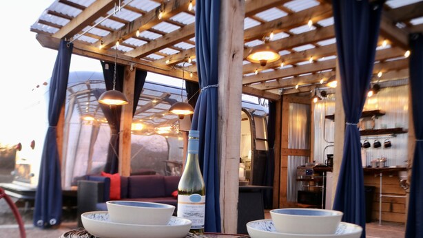 A cozy outdoor seating area with wicker coasters, a bottle of wine, and plates on a table. - Hocking Hills Airstream & Outdoor Living (McArthur)