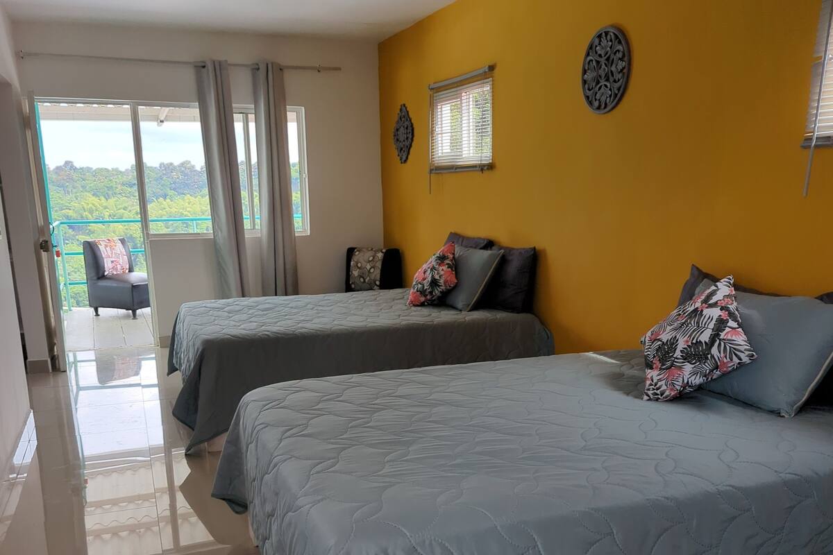 Une chambre d’hôtel avec deux lits, un balcon offrant une vue agréable et un mur d’accent jaune.