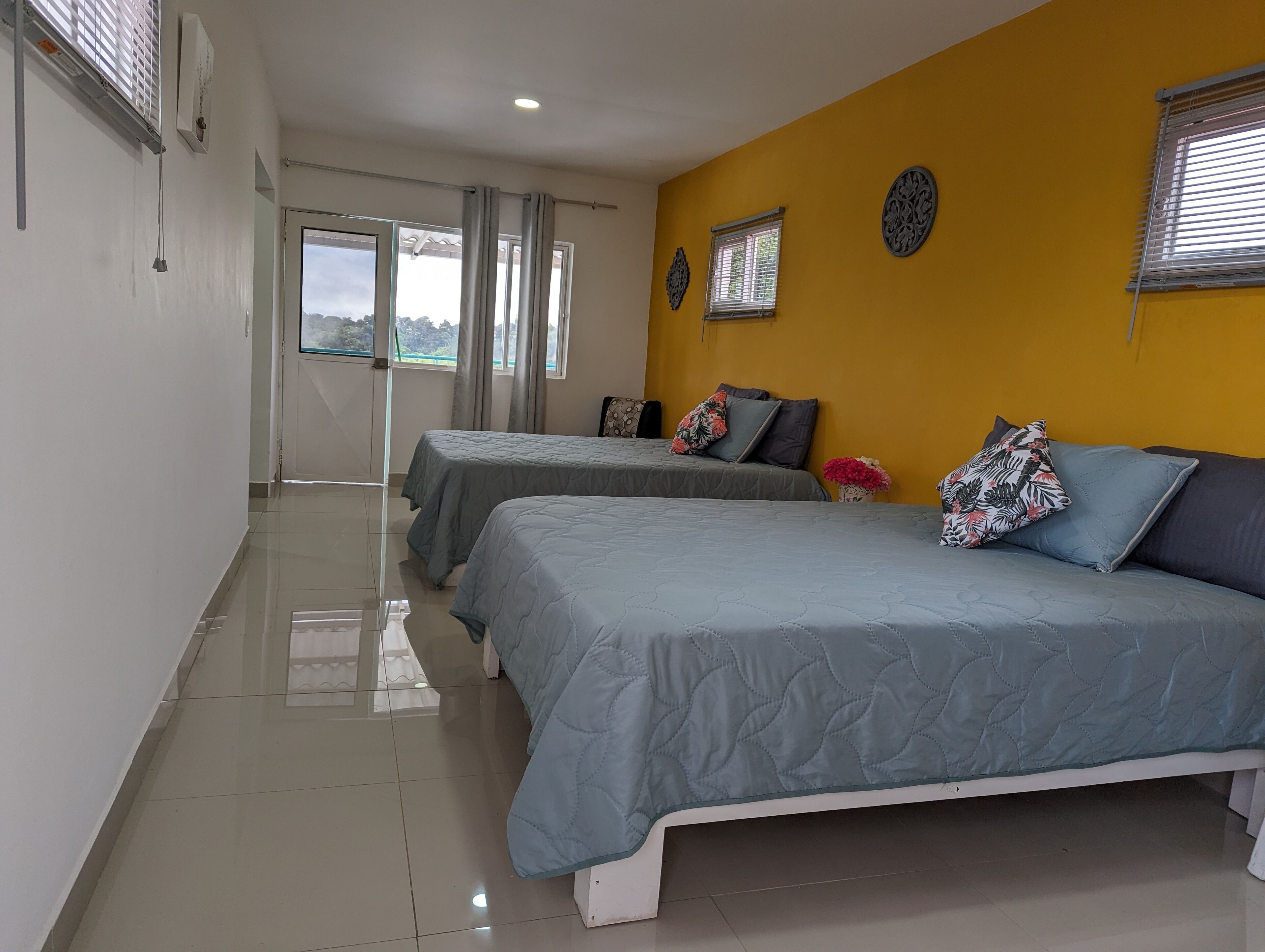 A hotel room with two beds, a yellow accent wall, and a view through the door.