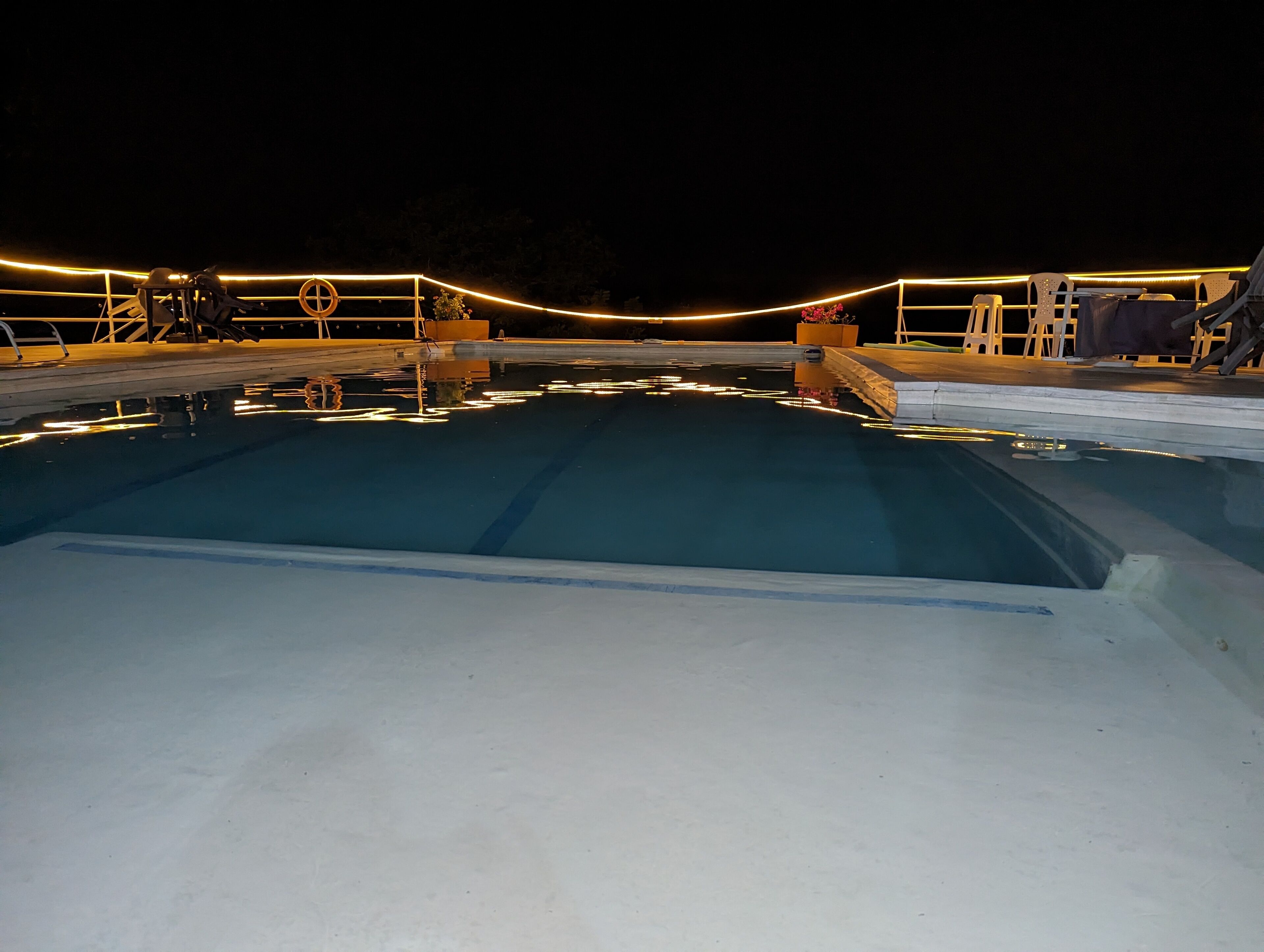 Une piscine dotée d’un espace de détente, entourée de rampes de protection et illuminée par des guirlandes lumineuses.