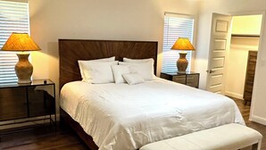A bedroom with a large bed, two bedside tables, a bench, and a door. - Austin UrbanScape, 5min to Kalahari water park! (Round Rock)