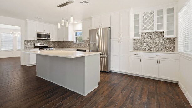 A modern kitchen with white cabinetry, a central island, stainless steel appliances, and a patterned backsplash. - Austin UrbanScape, 5min to Kalahari water park! (Round Rock)