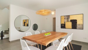Uma área de refeições moderna com uma mesa de madeira, cadeiras brancas e uma fruteira.