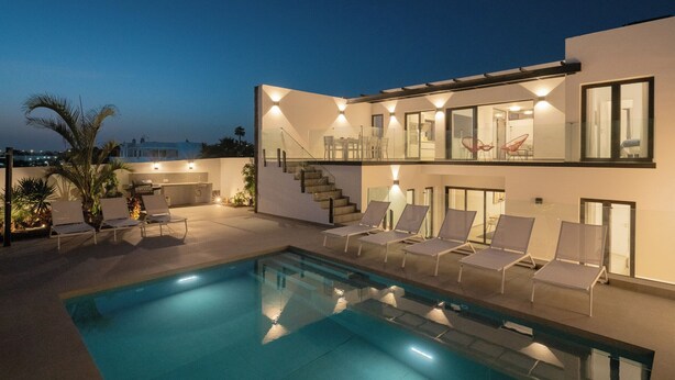 Uma casa moderna de dois andares com piscina, espreguiçadeiras e uma escadaria que leva ao andar superior.