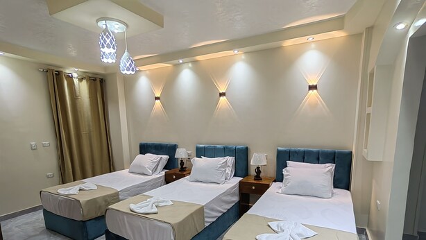 A hotel room with two single beds, a double bed, and a sofa bed. There are wall-mounted lights and a ceiling light fixture. - Gem & pyramids Front (Hadayek Al Ahram)