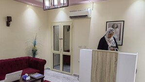 A reception area with a red sofa, a wooden desk, a laptop, and a patterned rug. - Gem & pyramids Front (Hadayek Al Ahram)