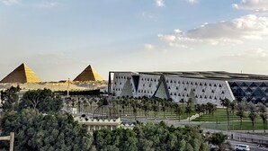 A view of the pyramids with a modern building in the foreground. - Gem & pyramids Front (Hadayek Al Ahram)