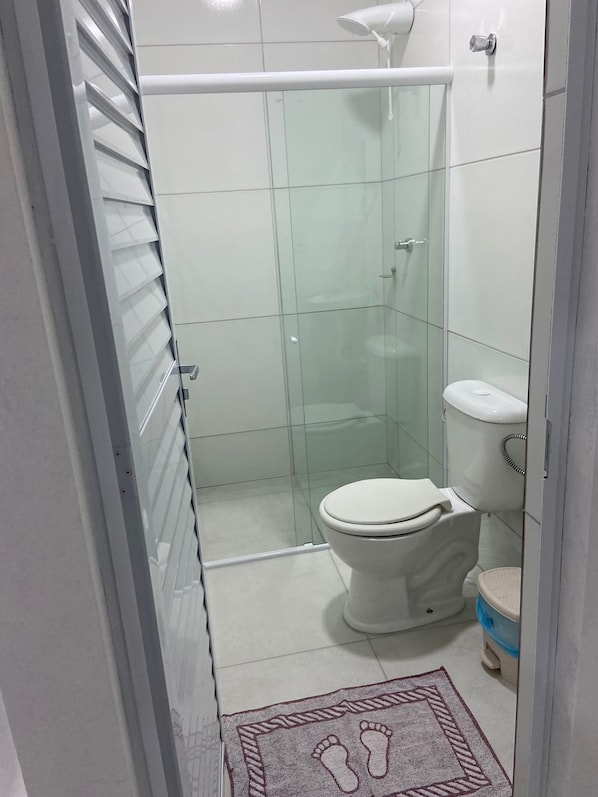 Baño con ducha de mampara de vidrio, inodoro y una alfombra pequeña con huellas.
