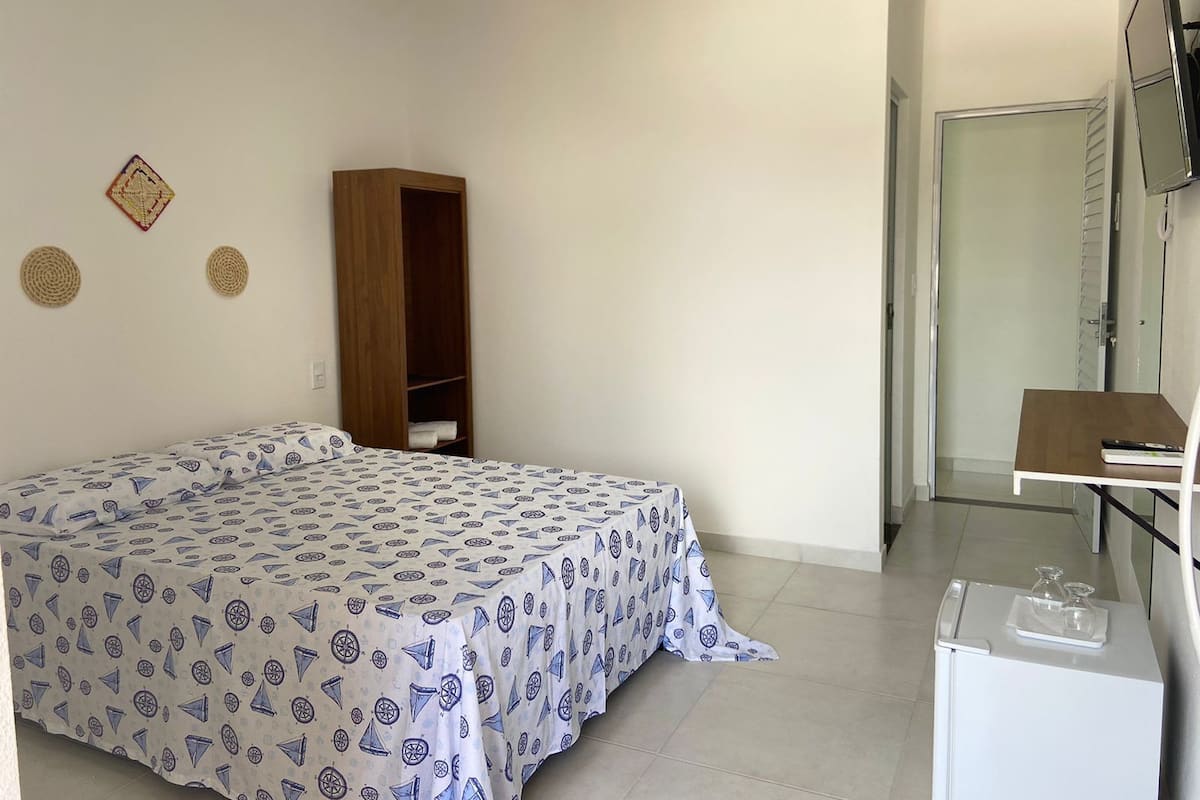 Ein Schlafzimmer mit einem Bett, einem Holzschrank, einem kleinen Tisch mit Spiegel und einer weißen Kommode.