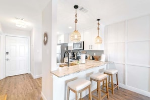 A modern kitchen with white cabinetry, a marble island with bar stools, and pendant lighting.
