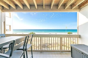 A balcony with a view of the ocean, a table, chairs, and a heater.