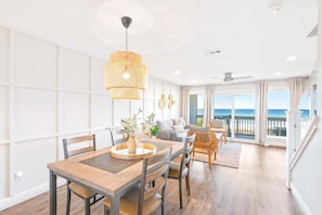 A modern living room with a dining area, large windows, and a view of the ocean.