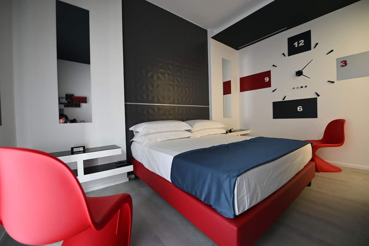 A modern bedroom with a bed, a red chair, a white bedside table, and a wall clock.