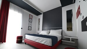 Una camera da letto moderna con un letto bianco e rosso, un poggiapiedi rosso, un comodino bianco e un'ampia finestra con tende rosse.