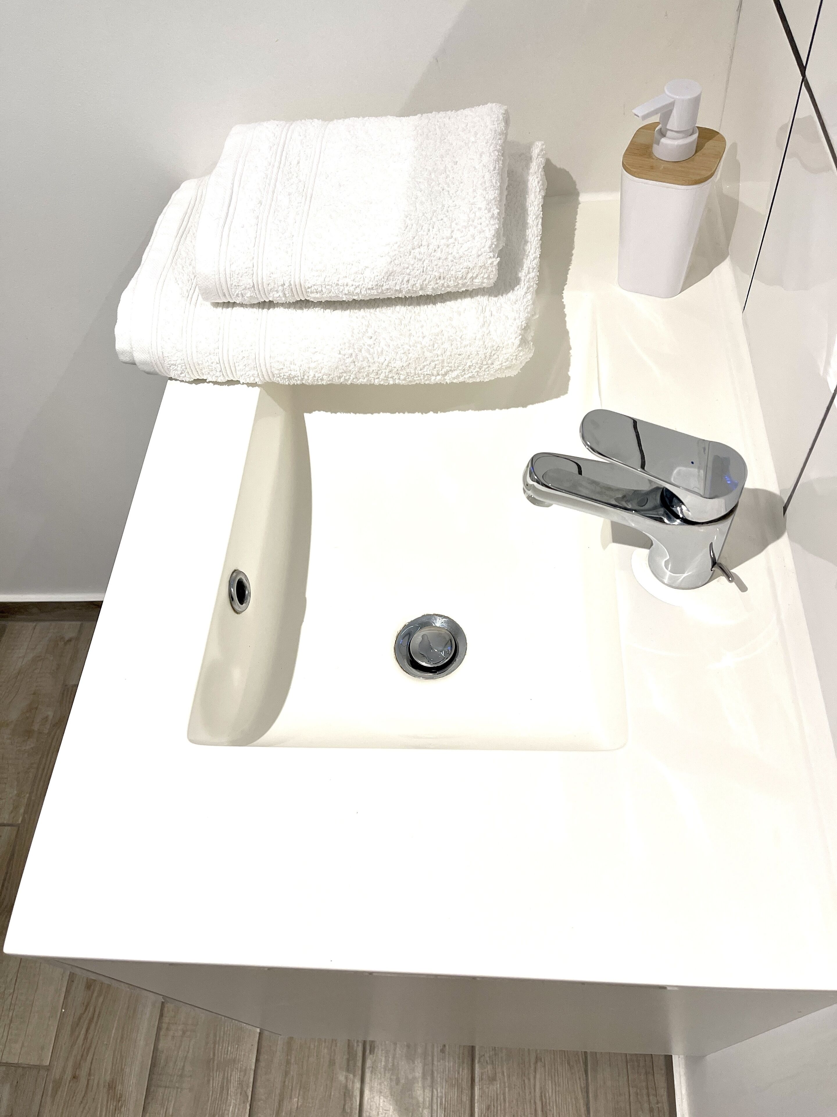 A white bathroom sink with a chrome faucet, a wooden soap dispenser, and a folded white towel on the sink's edge.