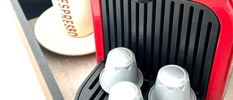 A red Nespresso coffee machine with three coffee capsules on the drip tray.