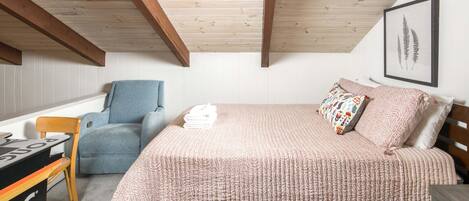 A bedroom with a bed, a chair, a desk, and a framed plant on the wall.