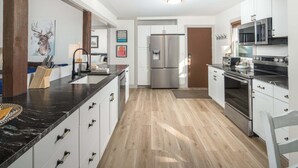 A modern kitchen with white cabinetry, a central island, stainless steel appliances, and a wooden floor. - Blue Ridge Mountain VIEWS | Pet Friendly | Near Boone & Blowing Rock (Boone)