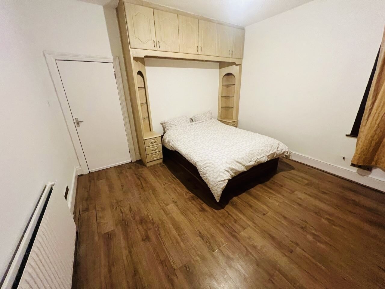 A bedroom with a bed, wooden flooring, a wardrobe, and a radiator.
