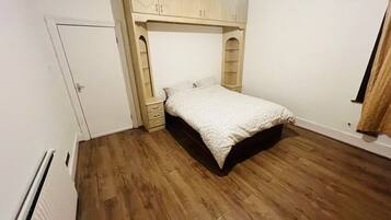 A bedroom with a bed, wooden flooring, a wardrobe, and a radiator.