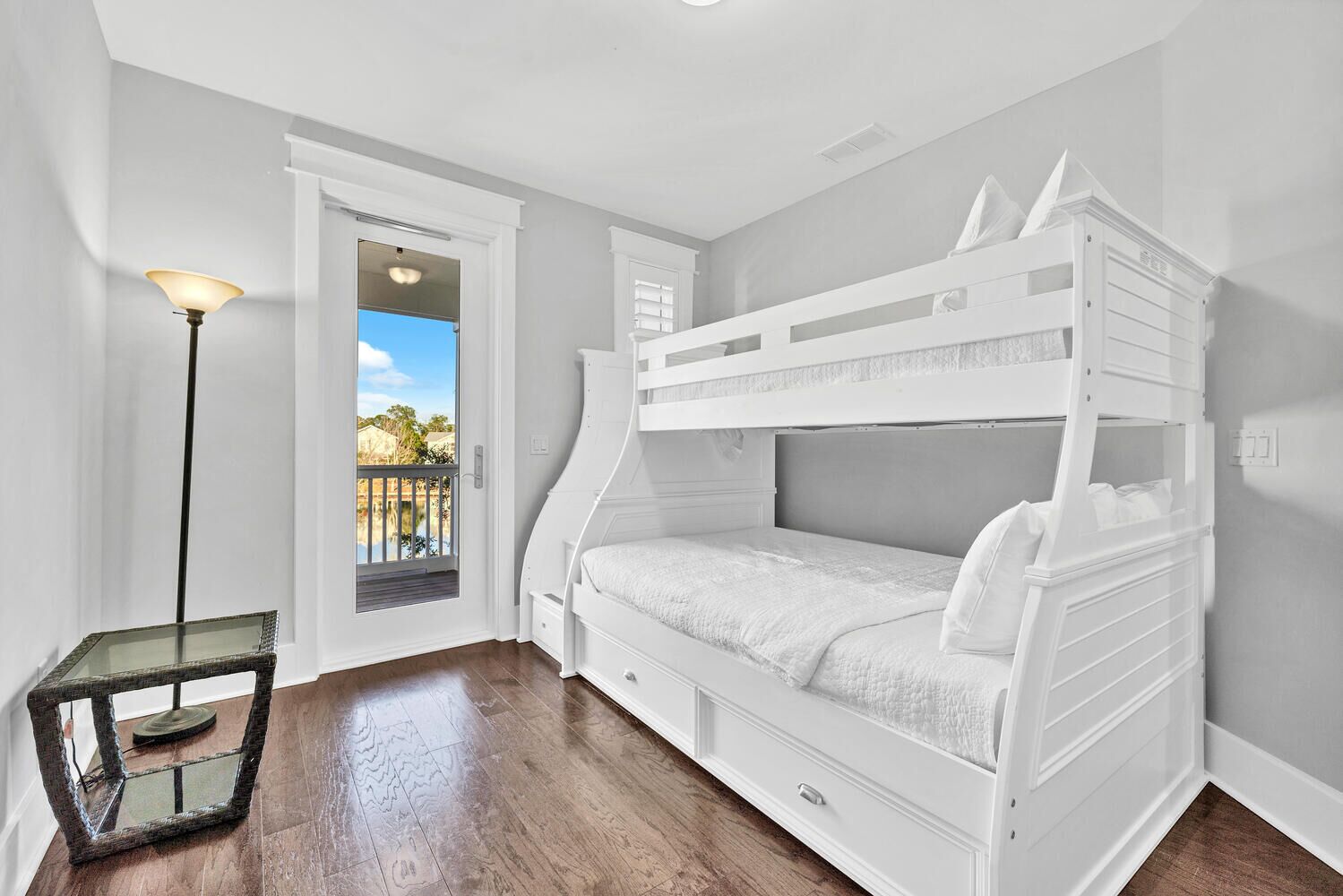 A bunk bed room with a glass table and a lamp, a door leading to a balcony, and a view of a pool.
