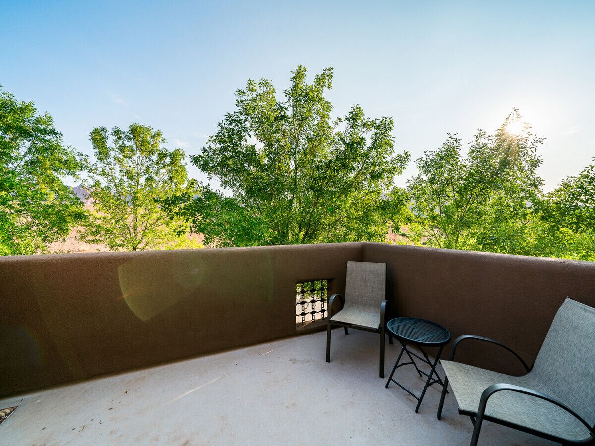 Un balcon avec un mur brun, deux chaises et une petite table ronde.