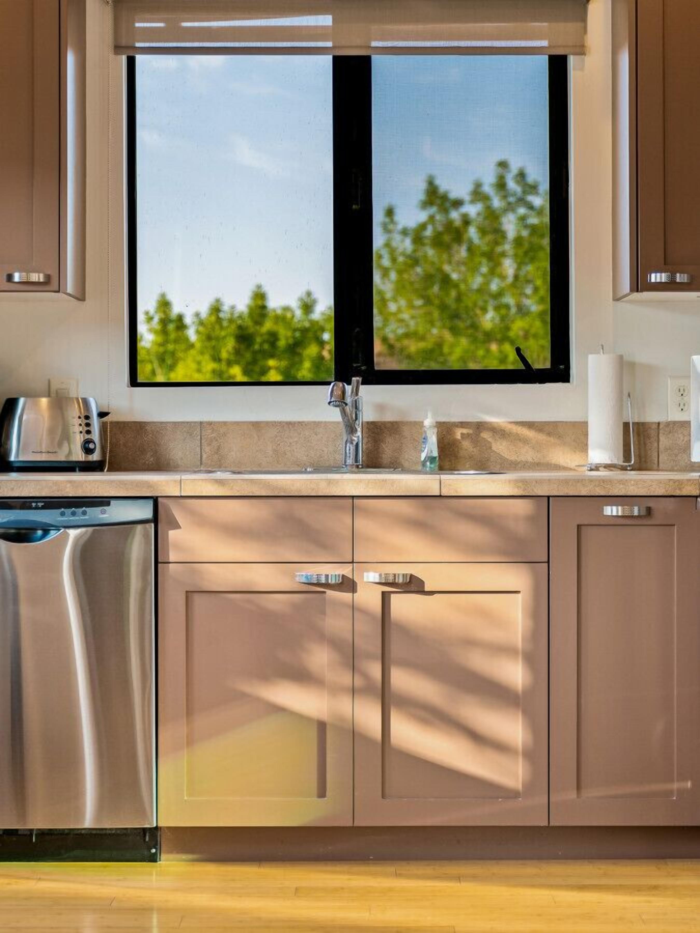 A kitchen with a double sink, a dishwasher, and a window with a view of trees.