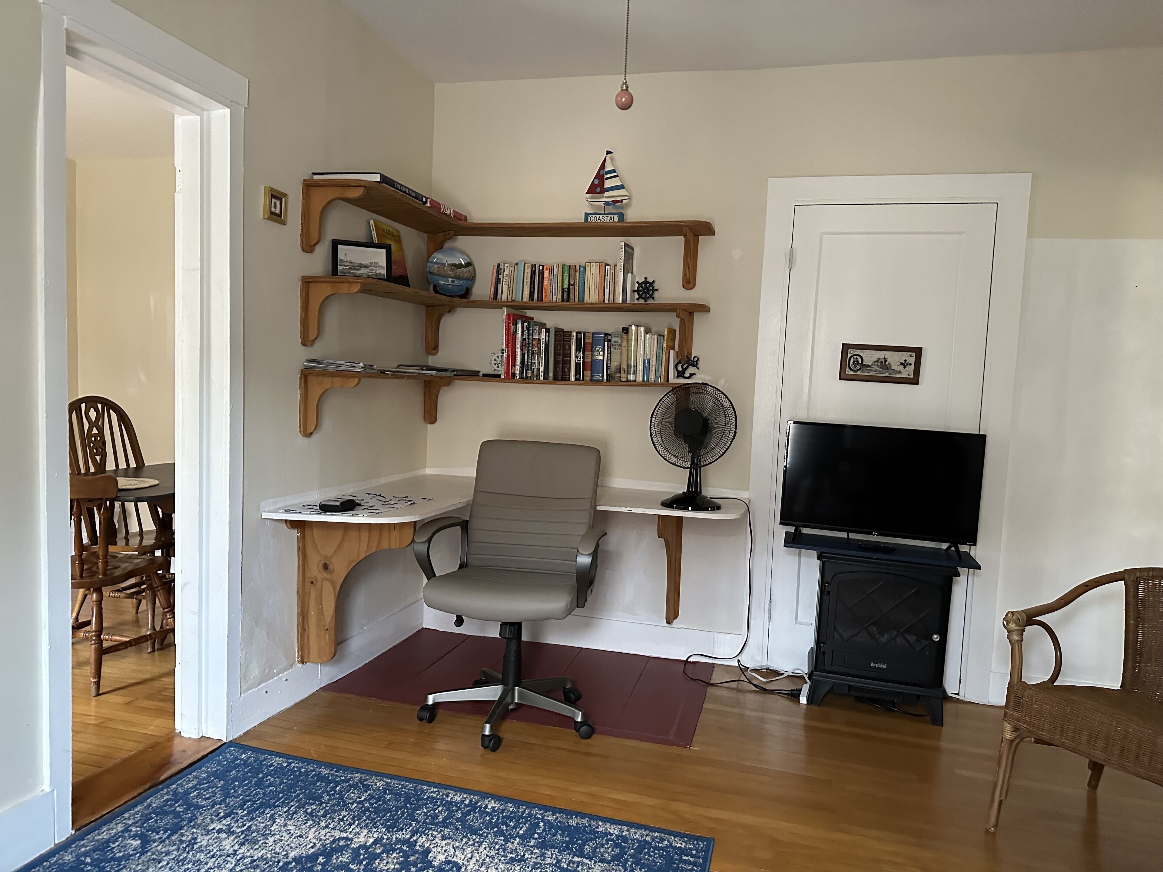 A living room with a wooden desk, a grey office chair, a bookshelf, a television, and a fireplace.