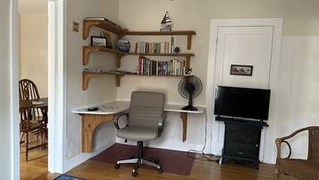 A living room with a wooden desk, a grey office chair, a bookshelf, a television, and a fireplace.