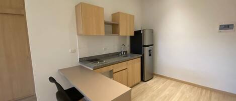 A small kitchen with a single sink, a refrigerator, and wooden cabinets.