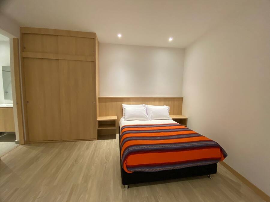 A bedroom with a bed, a wooden wardrobe, a nightstand, and a built-in shelf.