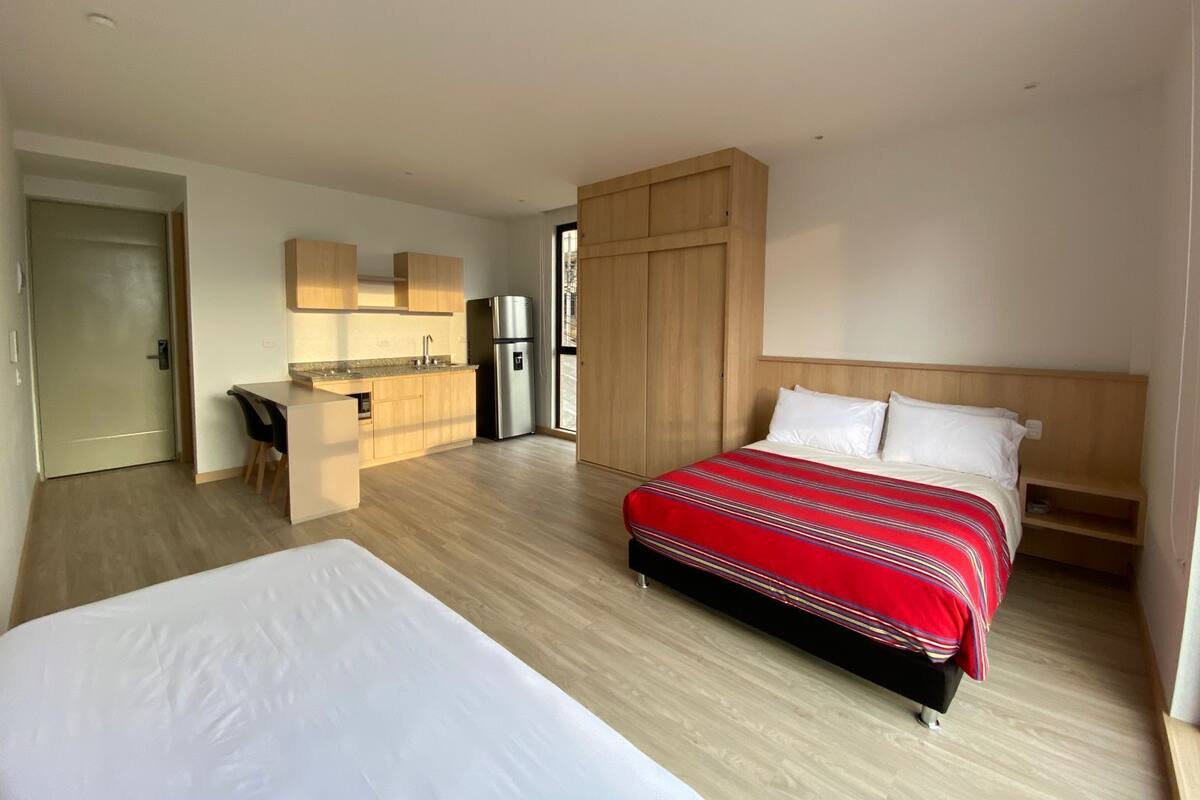 A modern hotel room with a large bed, a small kitchenette, and a view of the city.