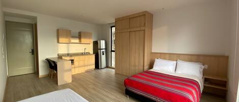 Una habitación de hotel moderna con una cama grande, una kitchenette pequeña y vistas a la ciudad.