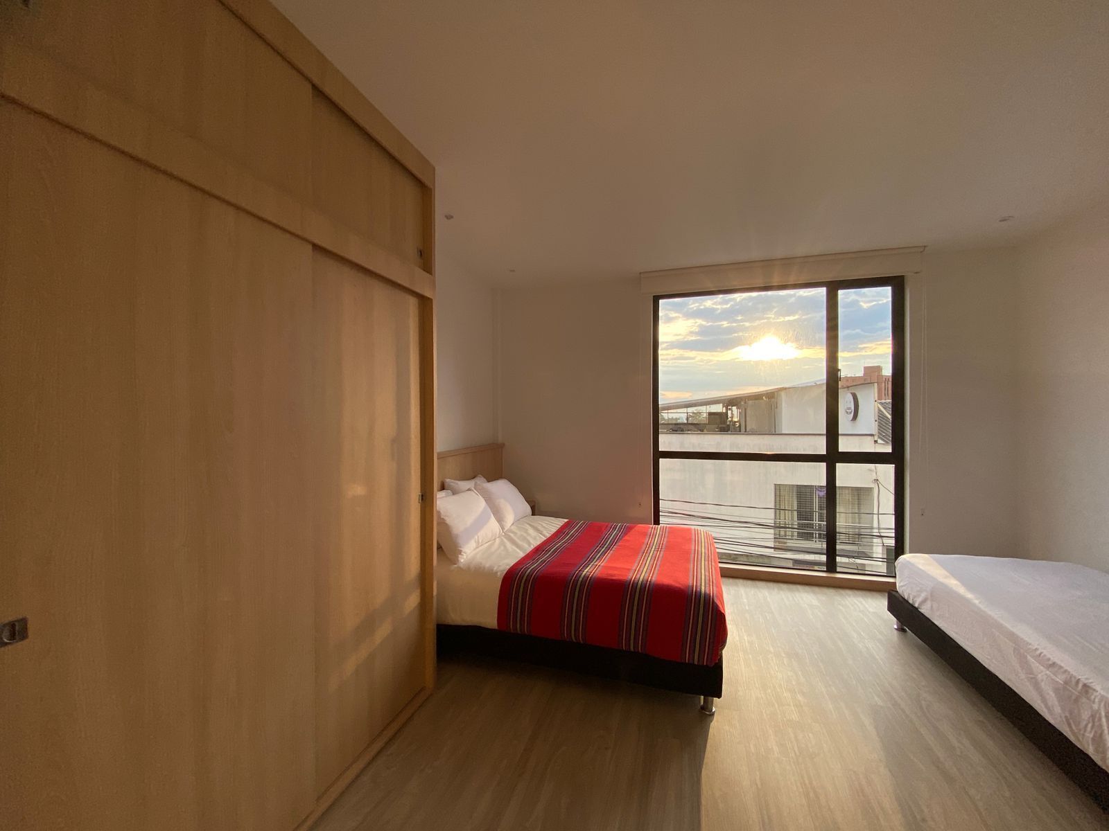 A bedroom with a bed, a wardrobe, and a large window with a view of buildings.