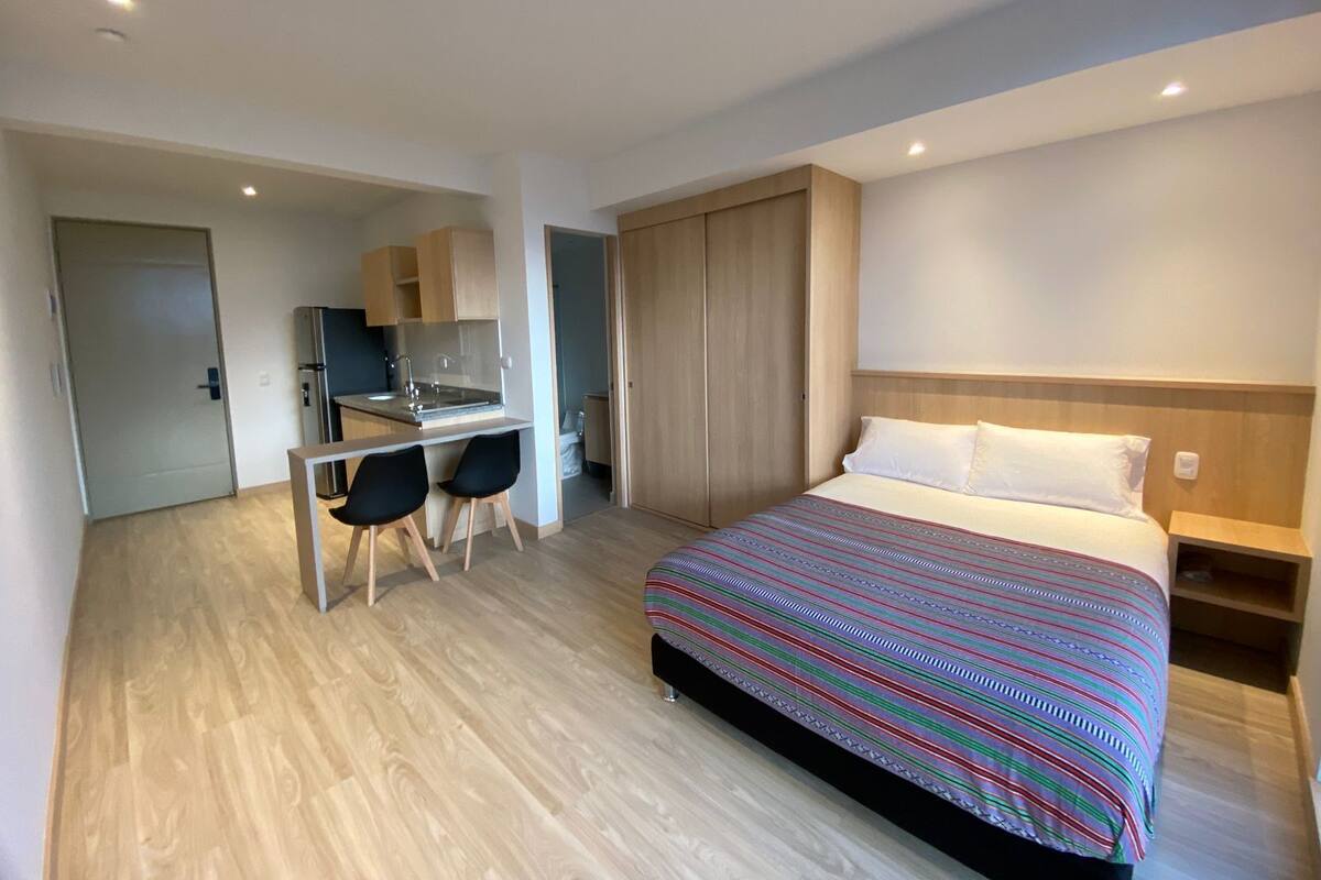A hotel room with a bed, a desk with two chairs, a kitchenette, and a wardrobe.