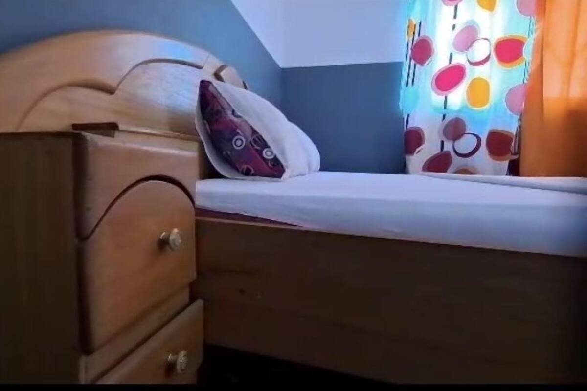 A wooden bed with a headboard, a pillow, and a colorful curtain.