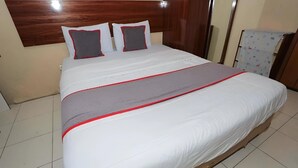 Un lit bien fait, avec une literie blanche rehaussée de touches de rouge, une tête de lit en bois et un sol carrelé.