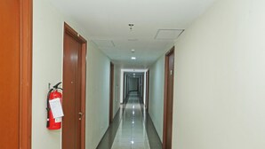 Un long couloir étroit, avec des portes en bois de chaque côté et un extincteur fixé au mur gauche.