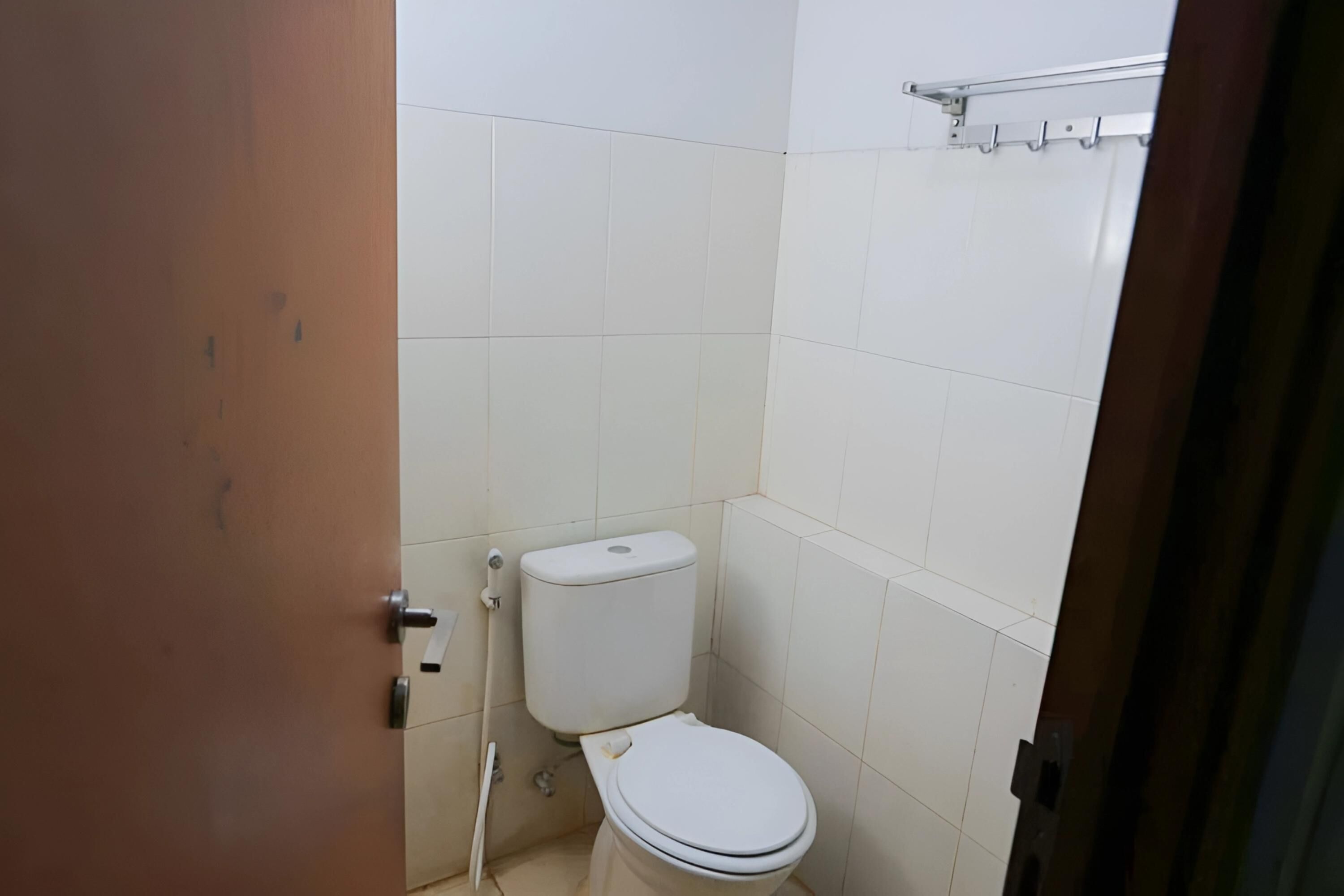 A small, clean bathroom with white tiles, a white toilet, and a wooden door.