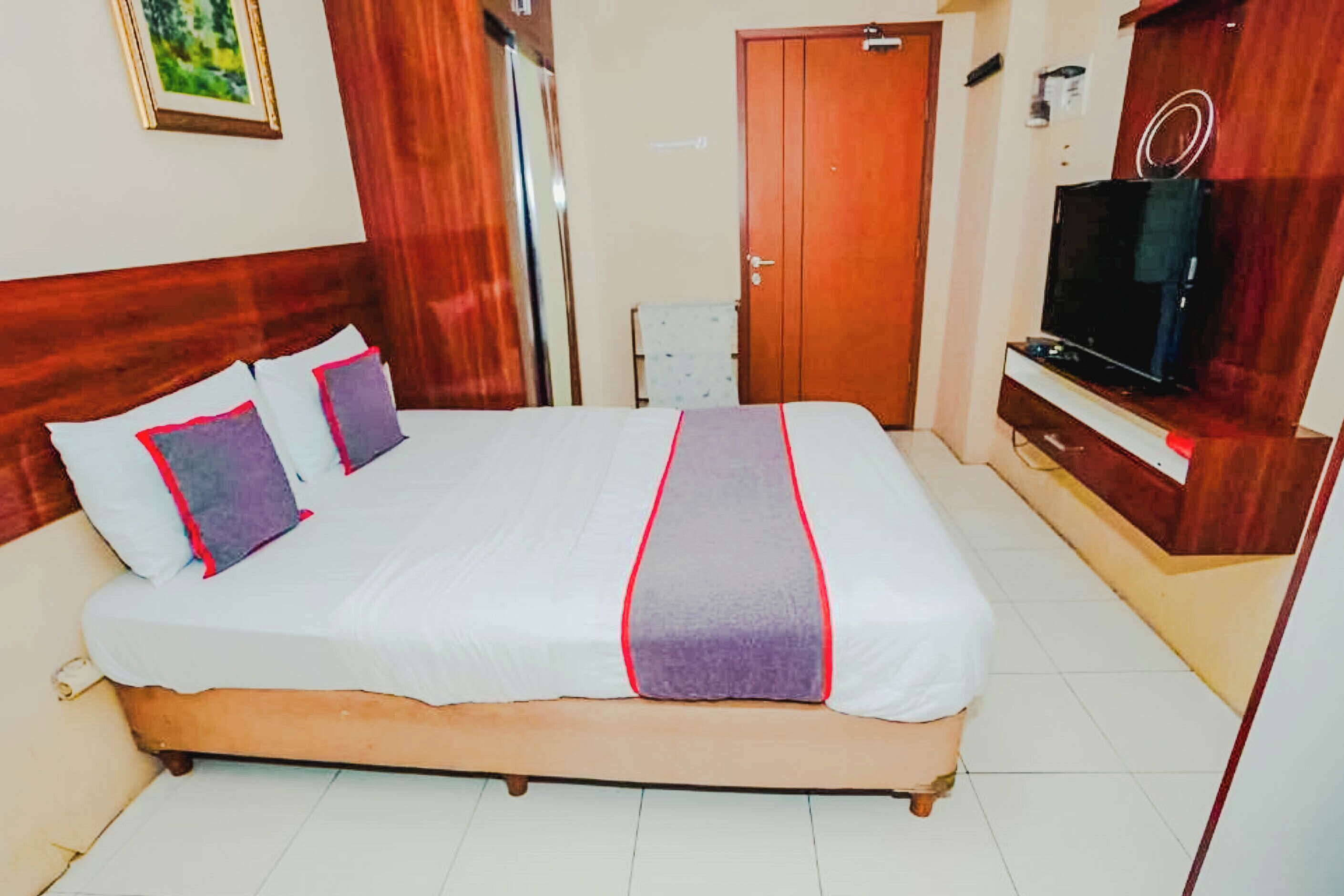 A hotel room with a large bed, wooden headboard, a television, and a wardrobe.