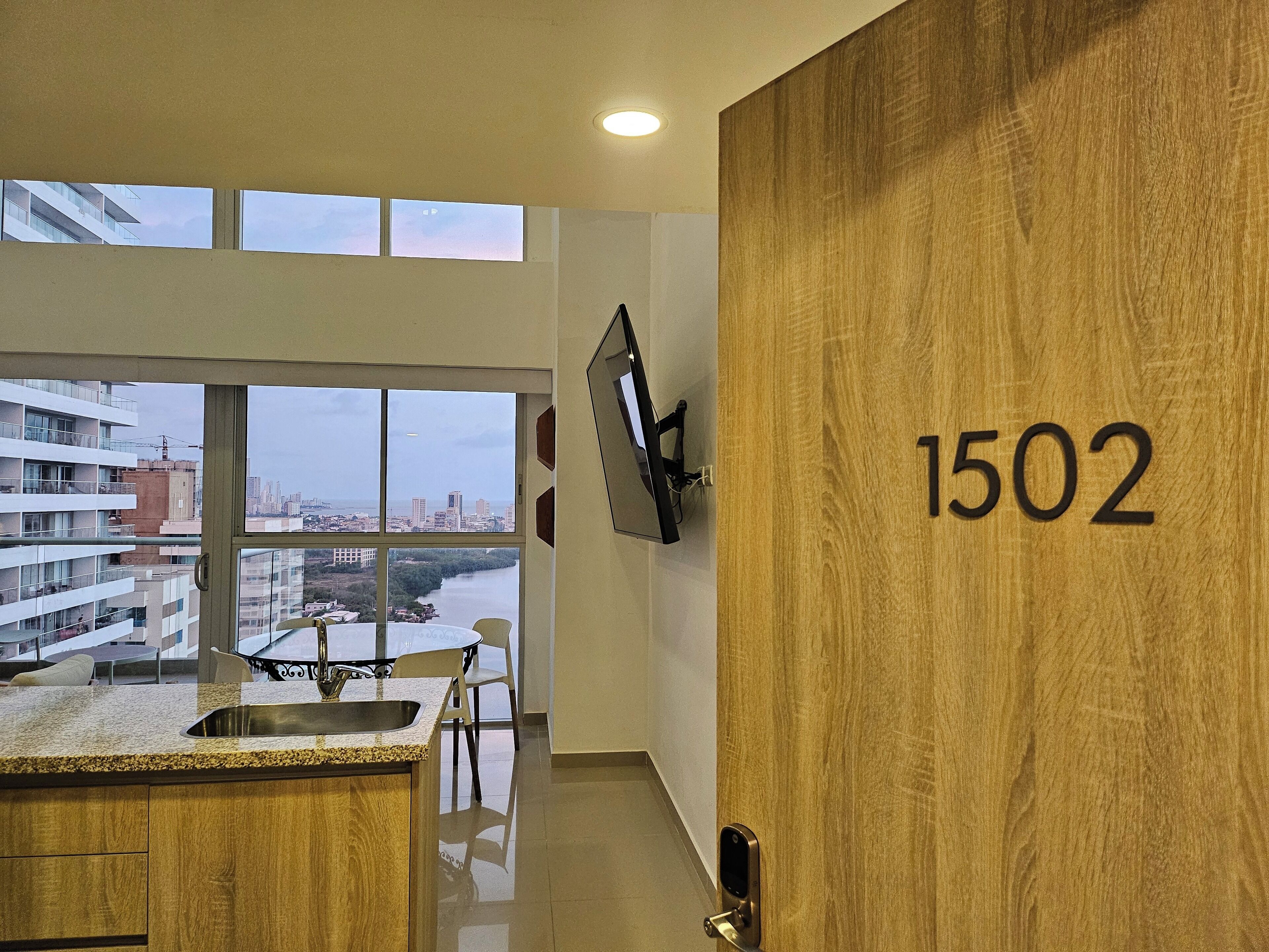 Une cuisine moderne dotée d’une grande fenêtre, offrant une vue sur la ville, et d’une porte en bois portant le numéro 1502.