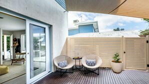 Une terrasse couverte avec deux fauteuils en osier et une petite table, une plante en pot et une porte-fenêtre coulissante donnant sur un espace intérieur.