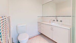 Une salle de bain avec des toilettes blanches, un lavabo et un miroir.