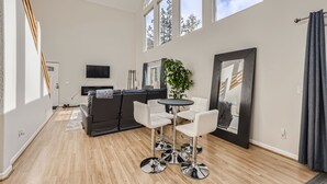 A modern living room with a sofa, a coffee table, and a TV. There are large windows and a plant. - Views, Rafting, Skiing, Tubing, Casinos, Zipline, Hiking, EV, Hot Tub (Idaho Springs)
