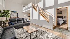 A spacious living area with a modern staircase, a leather sofa, a wooden coffee table, and a view into the bedroom. - Views, Rafting, Skiing, Tubing, Casinos, Zipline, Hiking, EV, Hot Tub (Idaho Springs)
