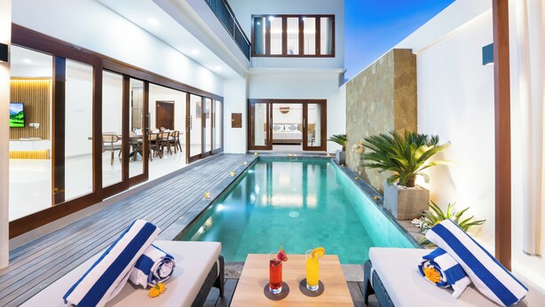 Un área de piscina interior moderna con muelle de madera, sillones de descanso y comedor.