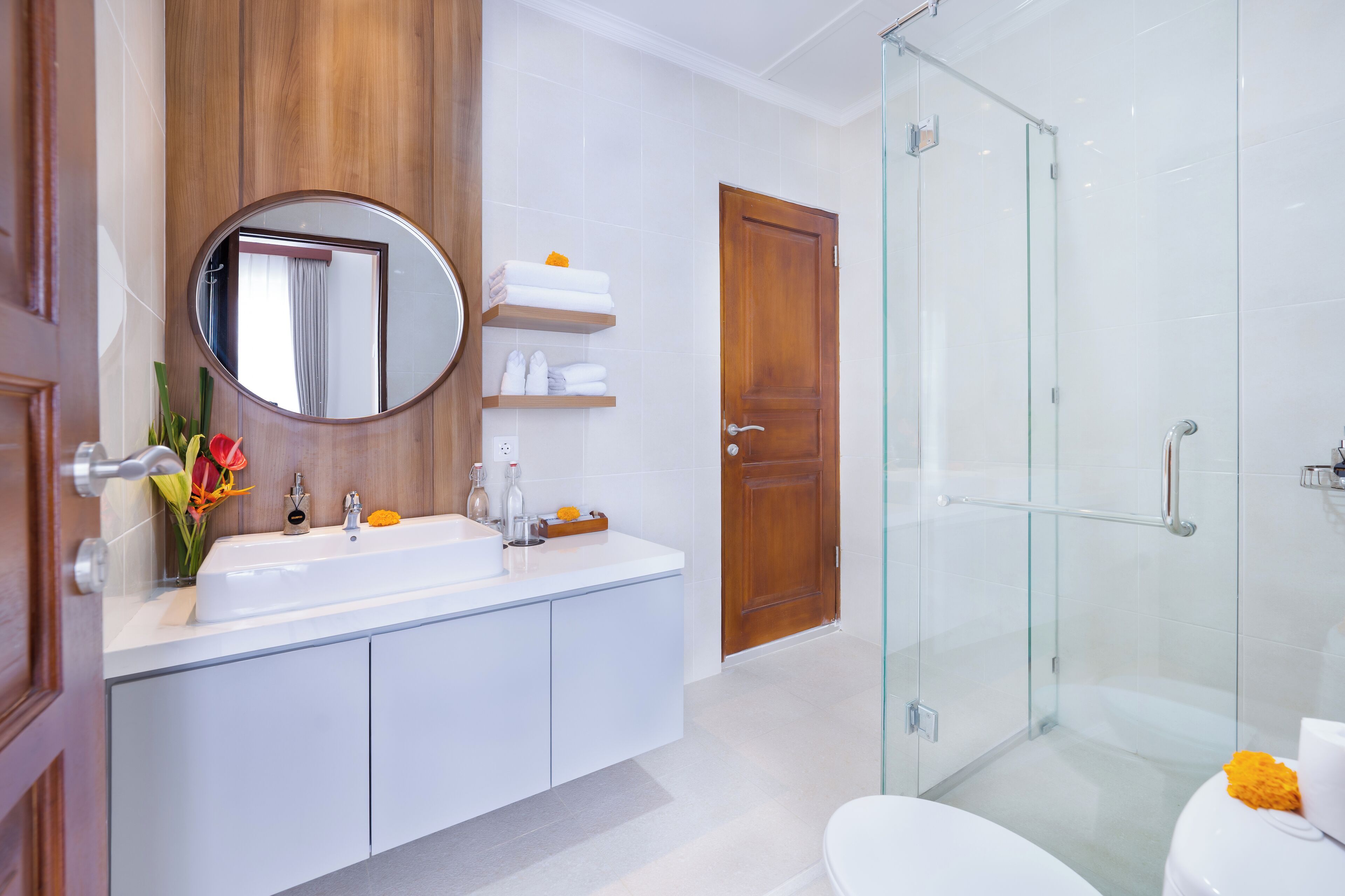 A modern bathroom with a glass shower enclosure, a white sink with a mirror, and a wooden door.