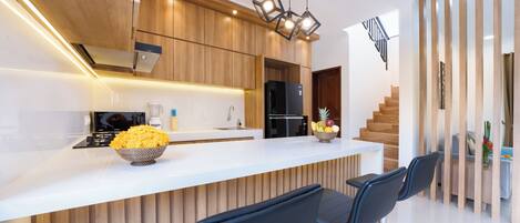 A modern kitchen with wooden cabinetry, a white countertop, and a built-in island with bar stools.