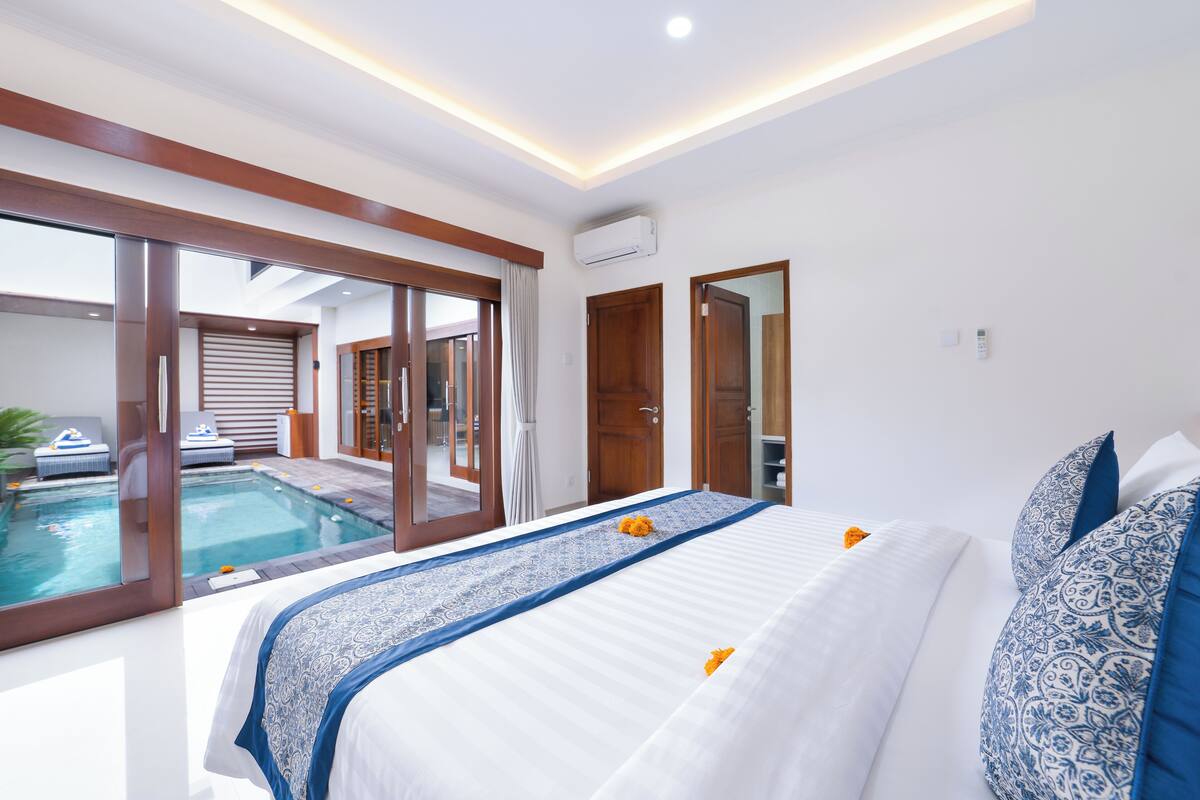 Hotelkamer met een groot bed, uitzicht op een zwembad en een schuifdeur naar een balkon.